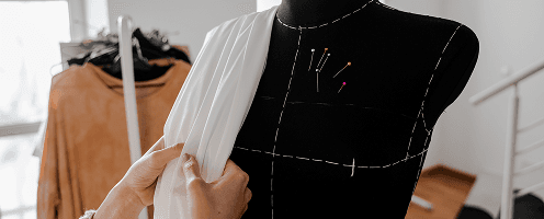 A woman laying fabric over a dress form.