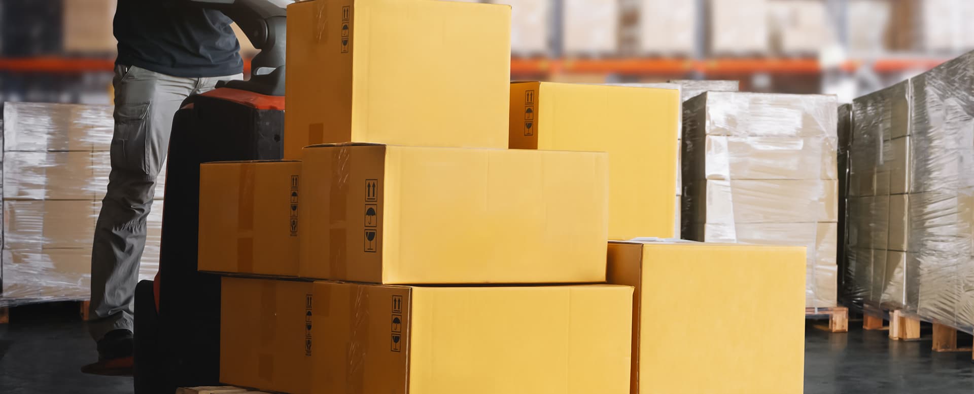 Warehouse worker transporting pallet of boxes with pallet jack
