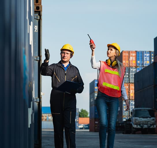 Logistics workers inspecting containers at shipping yard with radio and clipboard