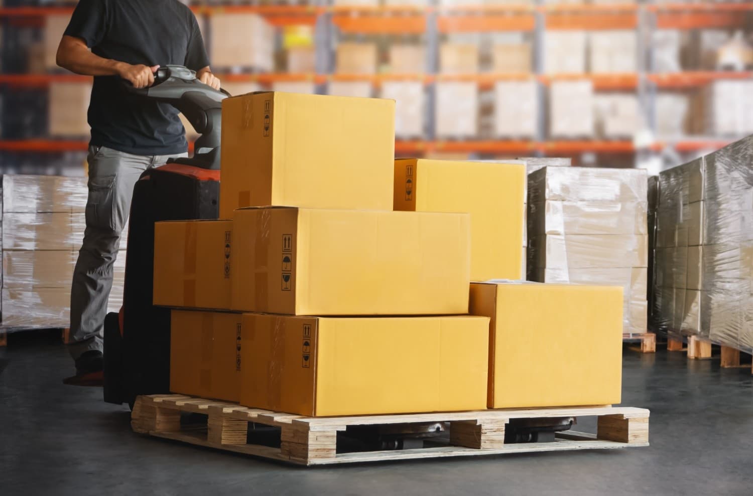 Warehouse worker transporting pallet of boxes with pallet jack