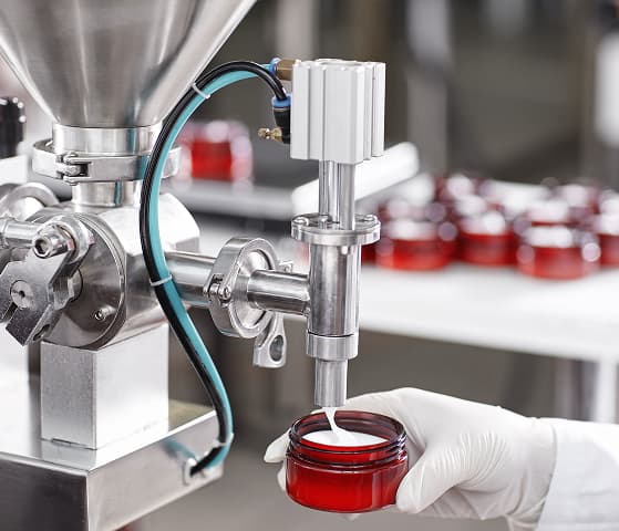 Factory worker filling red containers with beauty cream