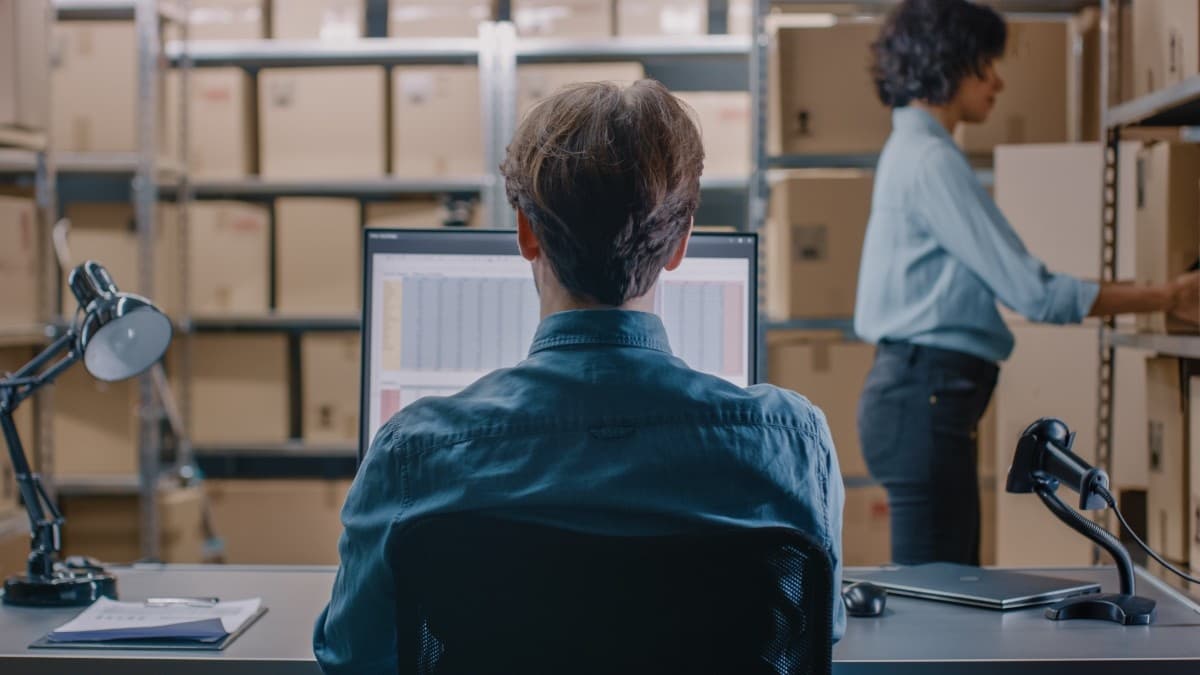 Warehouse staff managing inventory on computer with storage shelves in background
