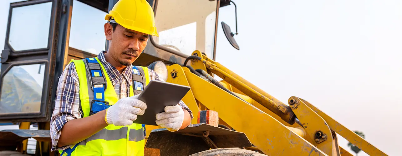 Man holding a tablet next to a farm loader.