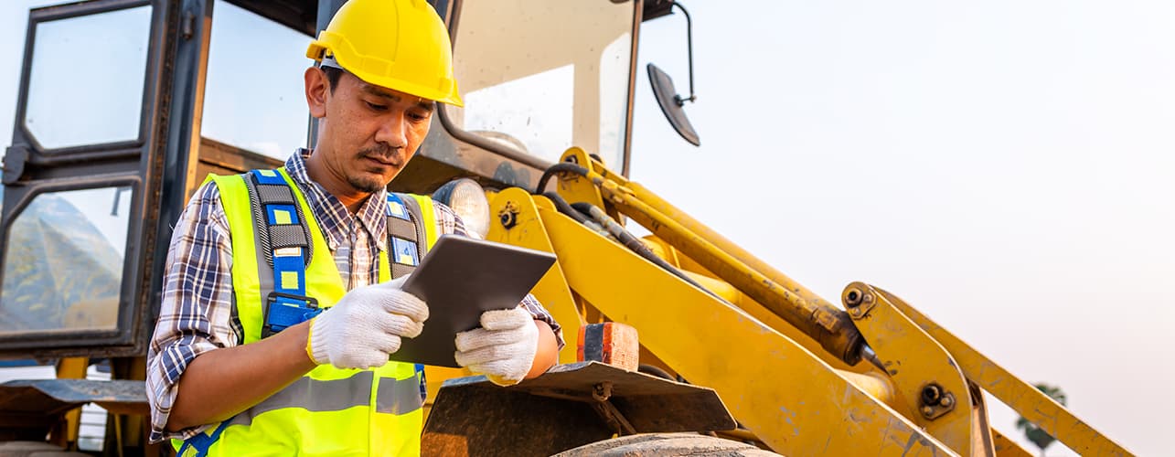 Man holding a tablet next to a farm loader.