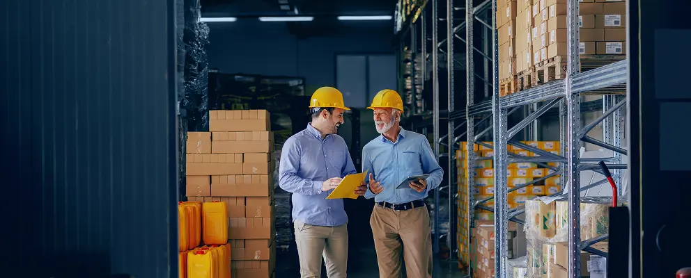 Business partners wearing safety helmets discussing operations in a warehouse